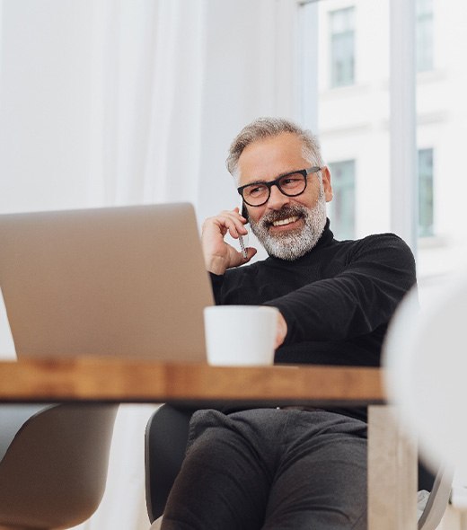 Man with glasses smiling while working on laptop