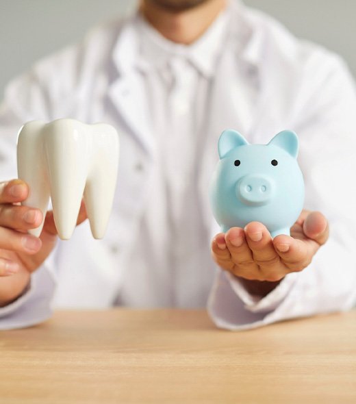 Man holding model tooth in one hand and blue piggy bank in the other