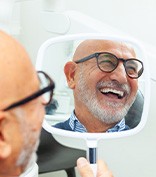 Older man smiling in the mirror at the dentist’s office