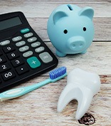 Calculator, model tooth, toothbrush, and piggy bank on wooden surface