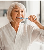 Senior woman in robe brushing her teeth