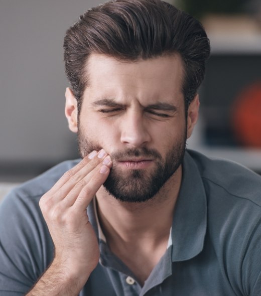 Man in need of emergency dentistry holding cheek in pain