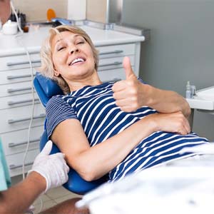 Woman smiling with thumb up sitting in dental chair