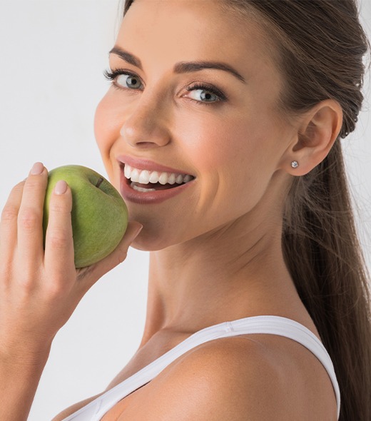 Woman eating a green apple after dental implant tooth replacement