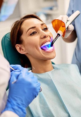 Dentist applying UV light to woman’s tooth-colored filling