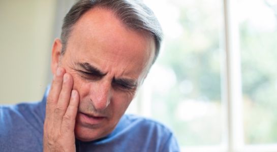 Man in need of restorative dentistry holding jaw in pain
