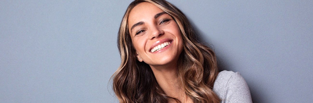 Woman in gray shirt smiling after teeth whitening treatment