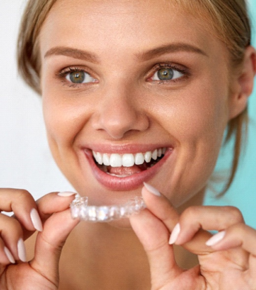 Woman smiling while holding teeth whitening tray