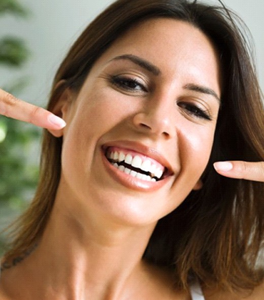 Smiling woman with veneers in Lubbock pointing to her teeth