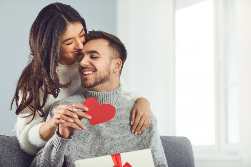 woman kissing a man holding a gift and a paper heart